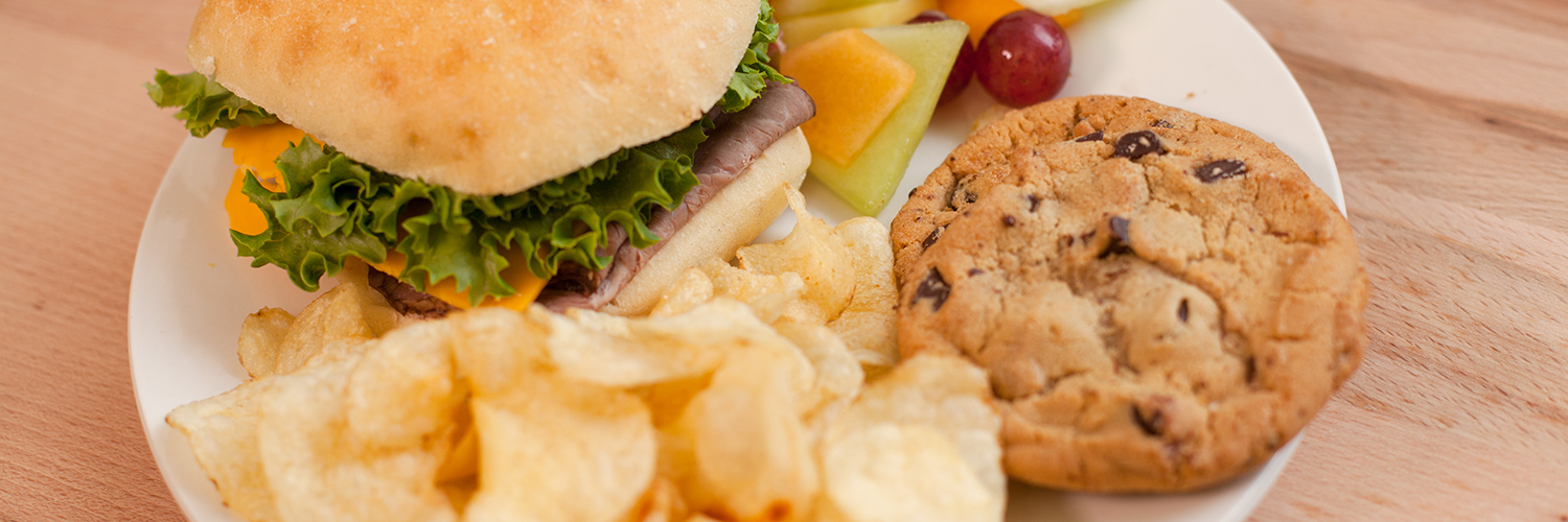 A sandwich, chips, a cookie, and fruit on a plate.