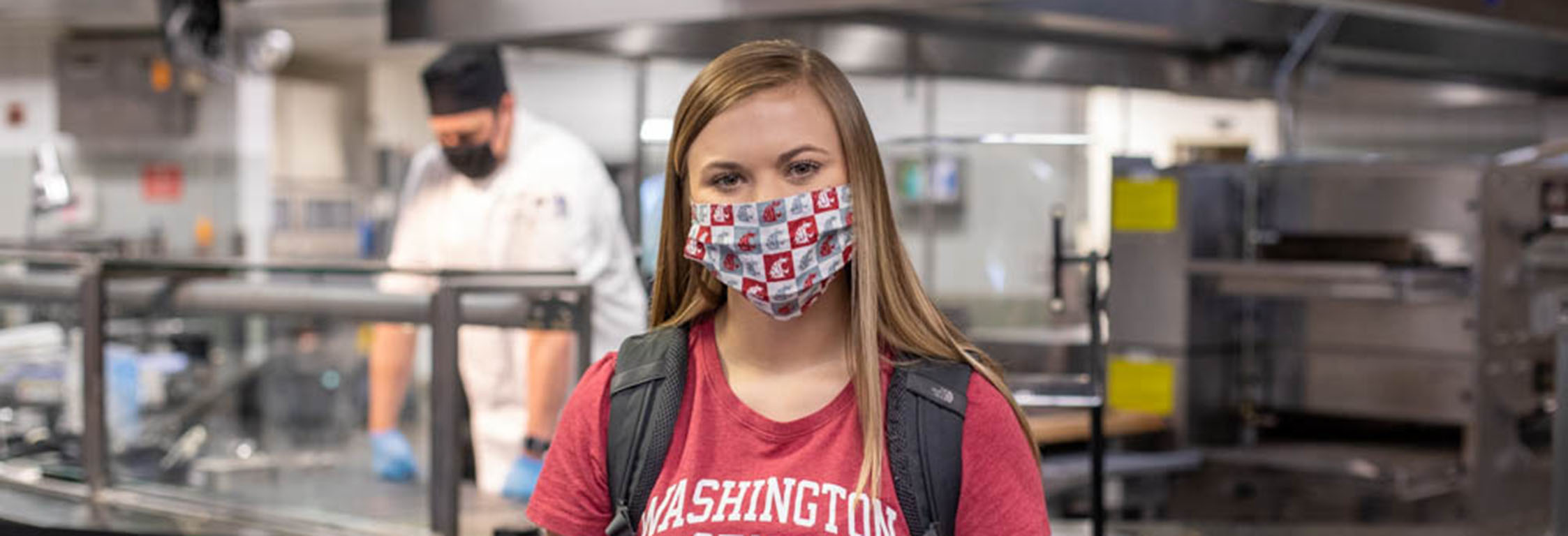 A student wearing a mask stands in front of a food counter at Southside Cafe.