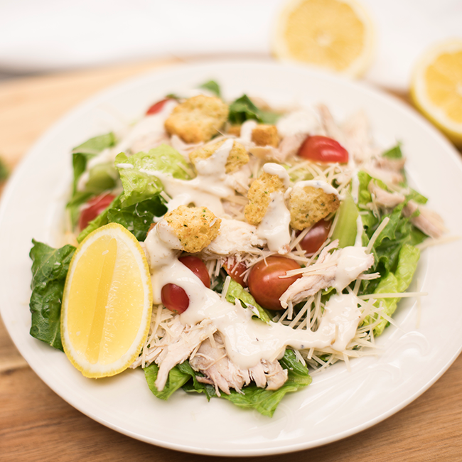 A chicken Caesar salad with lemon on a white plate.