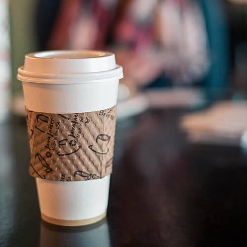 White coffee cup with brown sleeve on a black counter.