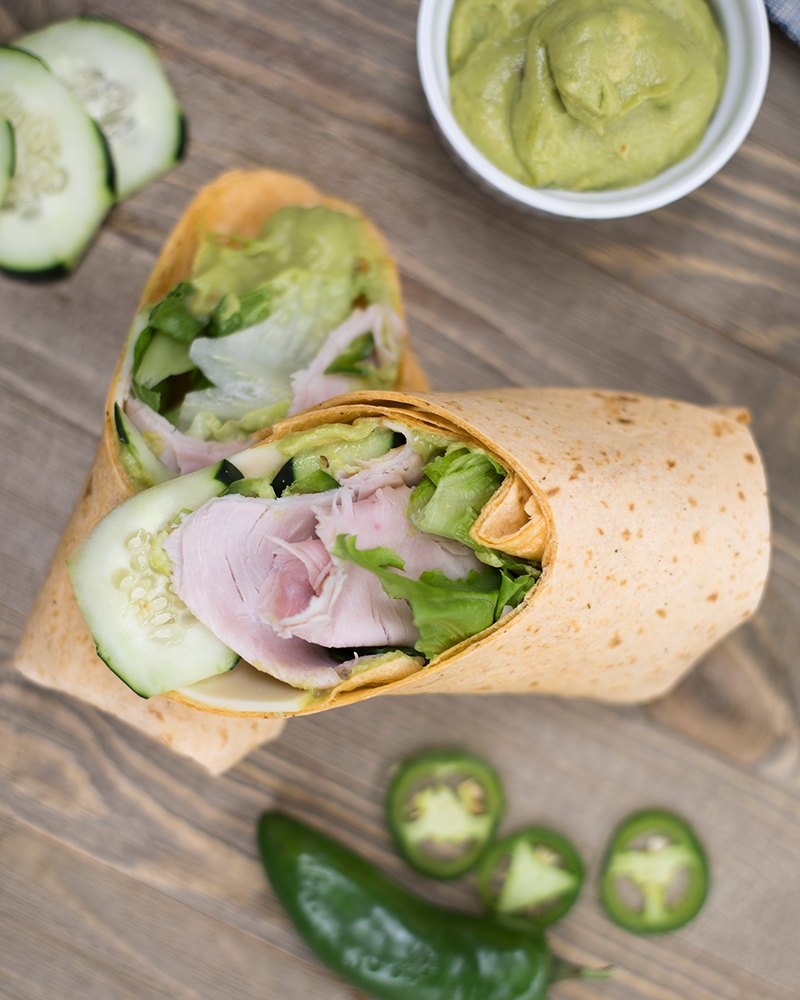 A turkey wrap cut in half with a side of guacamole.