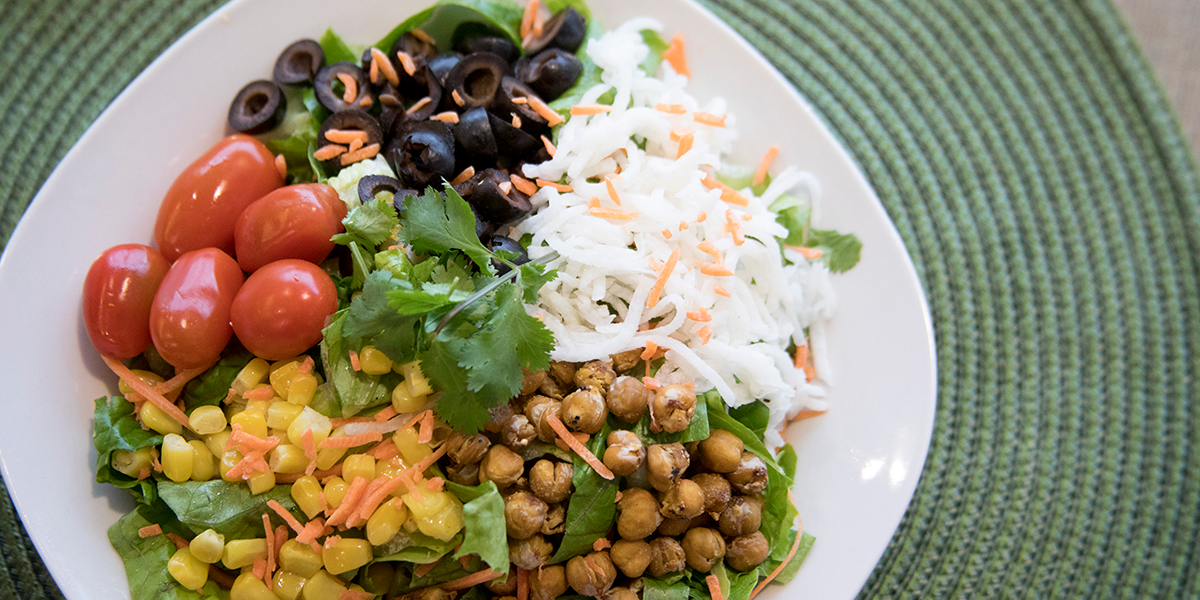 A salad with chickpeas, lettuce, corn, tomatoes, and olives.