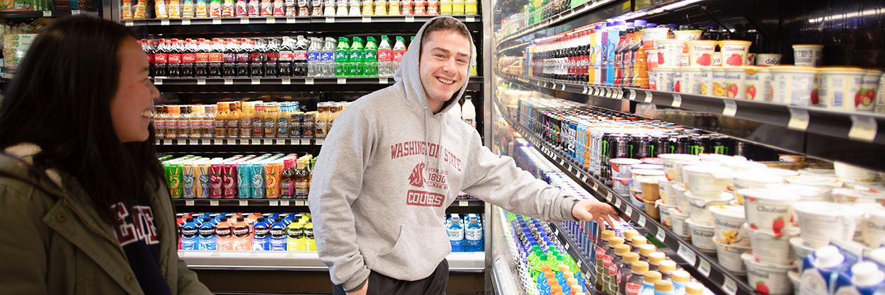 Student in grey WSU hoodie smiling while grabbing a chocolate milk at The Market cooler.