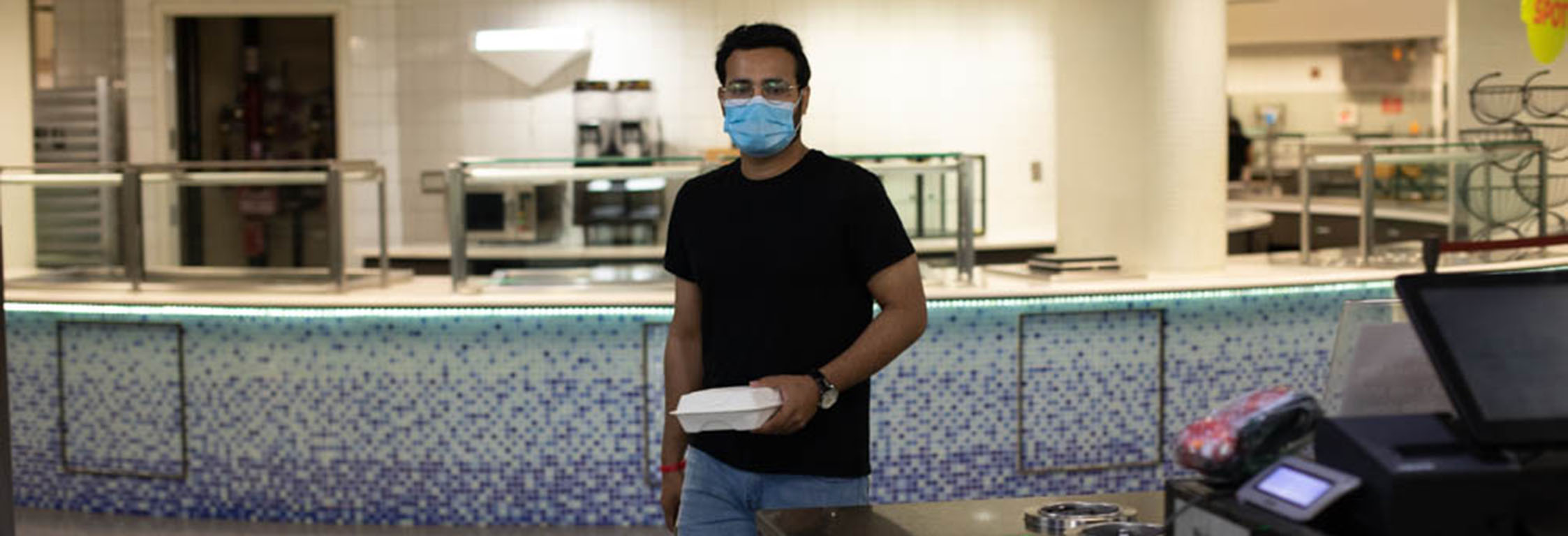 A student wearing a mask carries a to-go box at Southside Cafe.