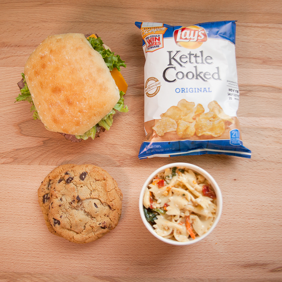 A sandwich, kettle cooked chips, a cookie, and pasta salad.