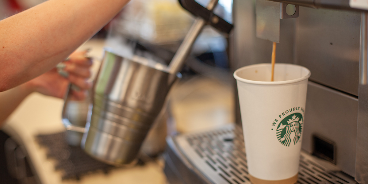 Coffee pouring into a white Starbucks cup while barista steams milk.