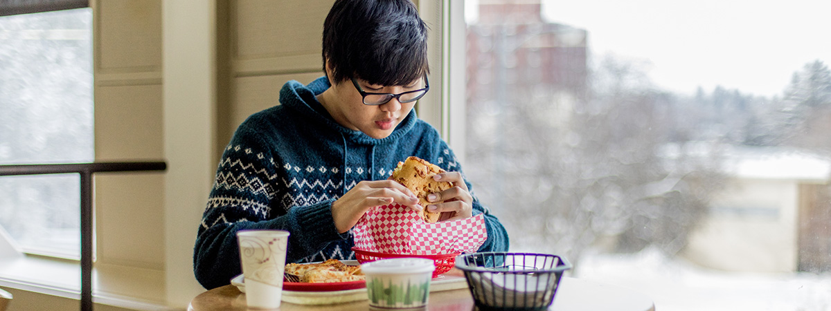 A guy sitting at a table about to bite into a sandwich.