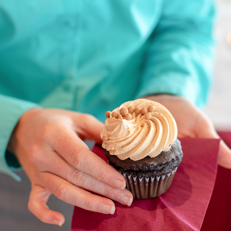 A chocolate cupcake in a persons hands.