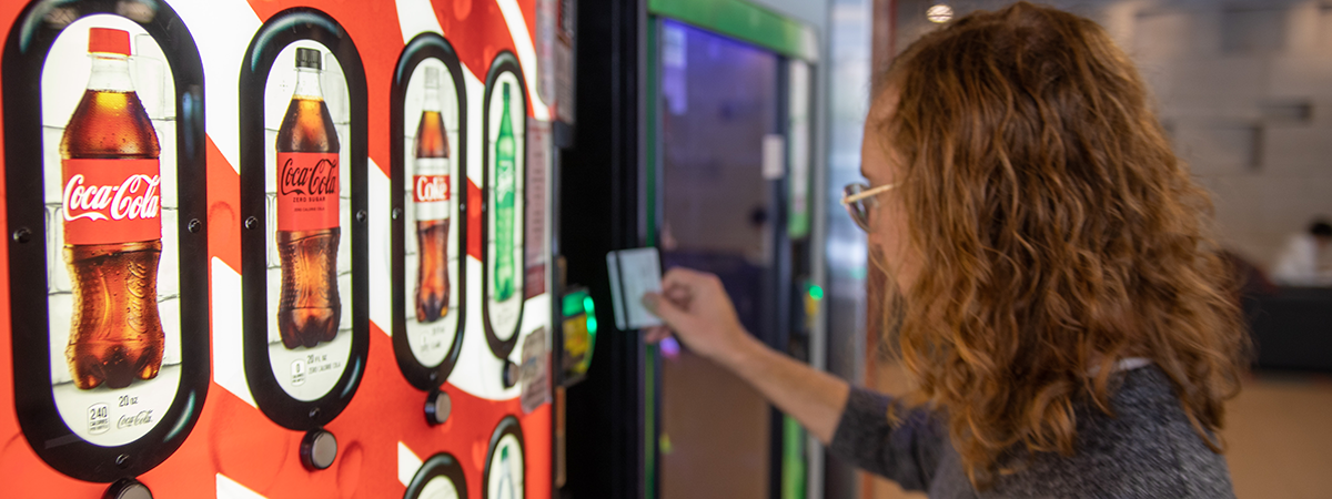 Person swiping card to get soda from vending machine.